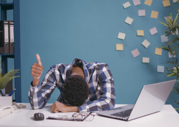 Travailleur épuisé posant la tête sur son bureau et faisant un signe de pouce levé et se sentant fatigué.