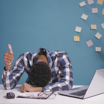 Travailleur épuisé posant la tête sur son bureau et faisant un signe de pouce levé et se sentant fatigué.