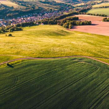 Image avec des champs de culture avec au loin un village, une rivière.